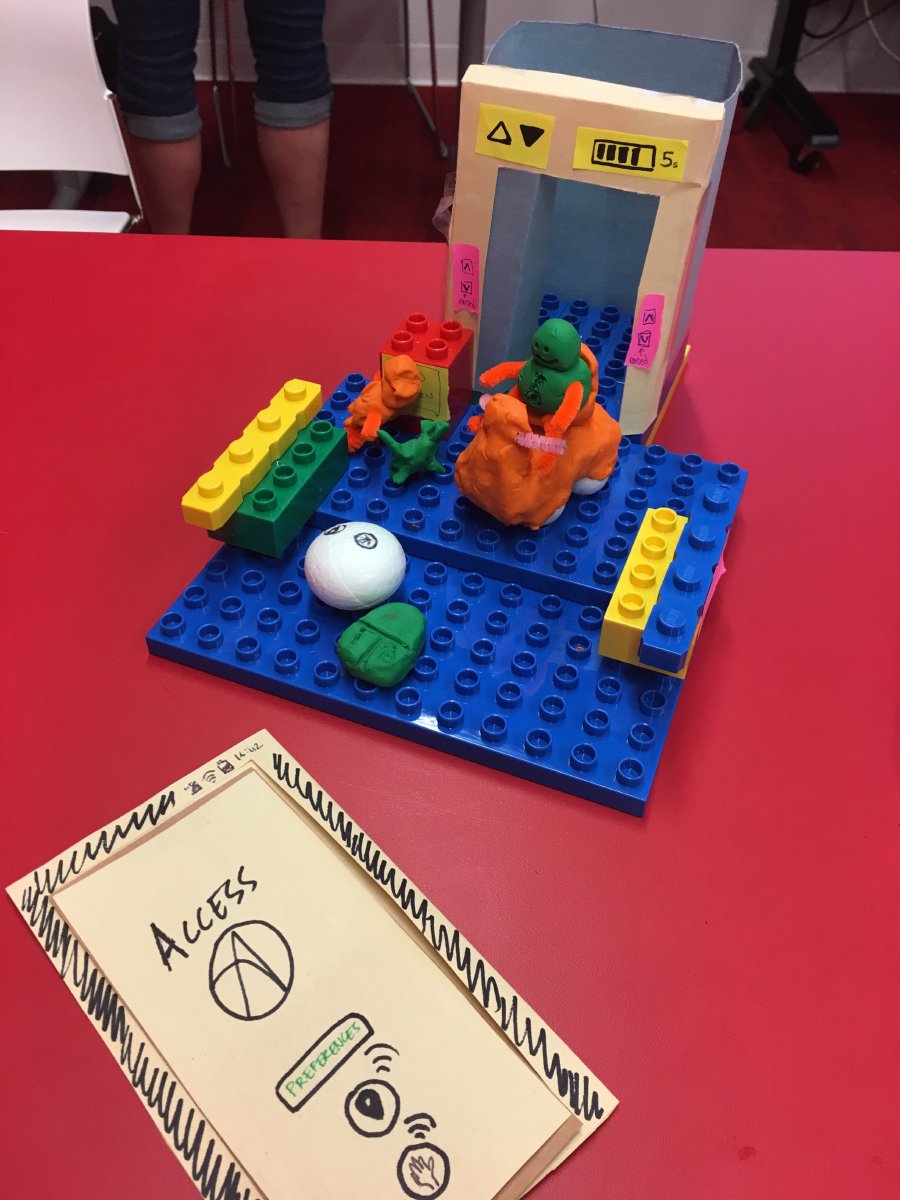 Pictured is group Assorted Barrier Busters prototype. They have used lego blocks to build a platform, craft paper to build an elevator cube and plasticine to create a mobility device, such as an electric scooter and a guide dog. The image also shows their proposed Access app prototype made with craft paper.